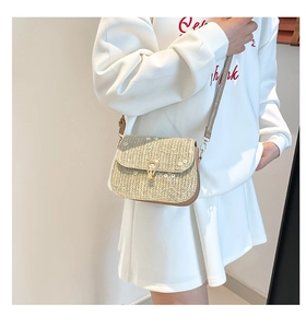 Detail of straw woven saddle bag featuring white floral embroidery and gold metal lock