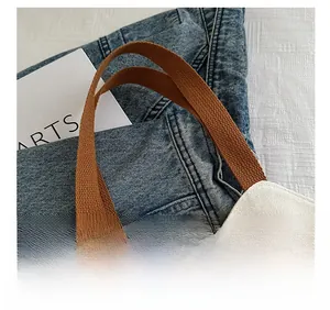 Detailed close-up of brown woven straps on cream canvas tote bag with reinforced stitching