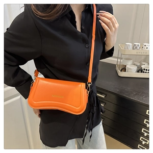 Detail of orange faux leather crossbody bag with asymmetric curved base and logo text
