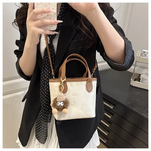 Detail of cream crossbody bucket bag with brown handles and plush monster charm