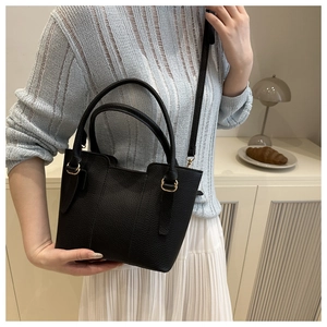 Detailed view of black pebbled leather bucket bag with gold hardware worn by a model