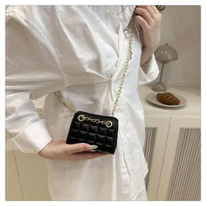 Close-up of mini black quilted crossbody bag with gold chain strap on a white shirt