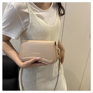 Detailed shot of beige leather shoulder bag featuring wavy flap and gold lettering
