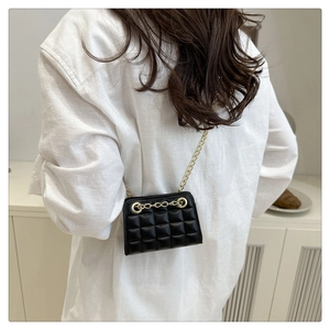 Detail of mini black quilted crossbody bag with gold chain strap on white linen top