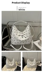 Détail du sac blanc texturé avec nœud, pendentif en forme de cœur et poignée argentée