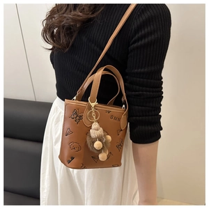 Brown bucket bag featuring butterfly print and plush charm shown on a shoulder strap