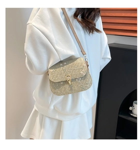 Close-up of beige straw saddle bag with white floral embroidery and gold metal clasp