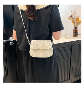 Close-up of woven straw crossbody bag with floral embroidery and golden metal clasp