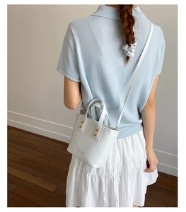 Close-up of white leather handbag with golden rivets and adjustable shoulder strap