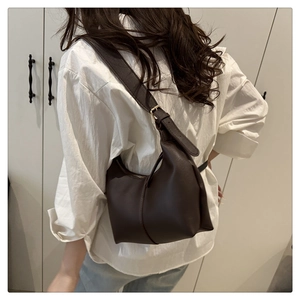 Detail of dark brown leather tote bag with adjustable wide strap shown on model's shoulder
