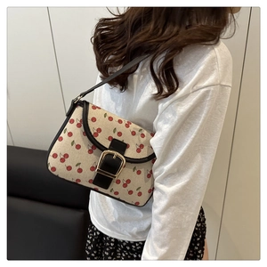 Close-up of cherry print underarm bag with black leather strap and large gold buckle