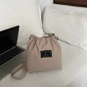 Minimalist khaki nylon drawstring bucket shoulder bag with black logo label on white surface