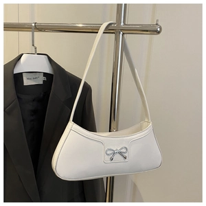 Close-up of a white patent PU baguette bag with a silver metallic bow decoration