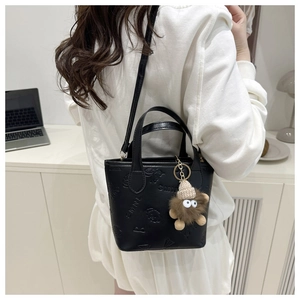 Detail of black textured bucket bag with SMNL embossing and plush toy charm accessory
