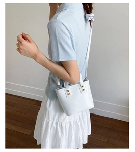 Detail of white leather bucket bag with gold stud accents and logo on textured surface
