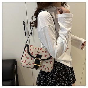 Detail of cherry print canvas underarm bag with black leather strap on a model