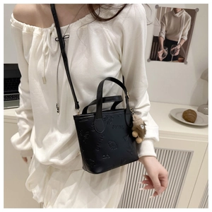 Close-up of black embossed bucket bag with butterfly motifs and a cute plush bear charm
