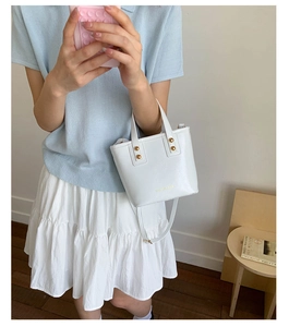 White minimalist bucket bag with gold studs shown in a casual lifestyle setting