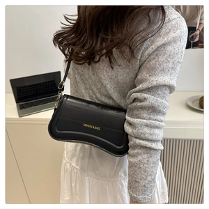 Detail showing glossy black leather shoulder bag with gold metal buckle and fashion logo