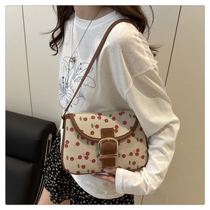 Crossbody wear of the cherry print canvas saddle bag with brown leather trim and buckle