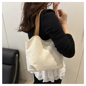 Detail view of cream canvas tote bag with contrast brown woven straps on a model's shoulder