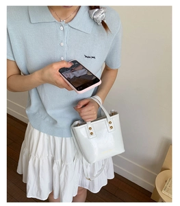 Close-up of white glossy mini tote bag with gold stud accents and matching shoulder strap