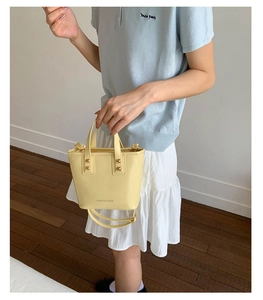 Close-up of yellow mini bucket bag with gold rivets and detachable shoulder strap