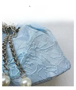 Detail of light blue satin bucket bag featuring floral embroidery and pearl pendants