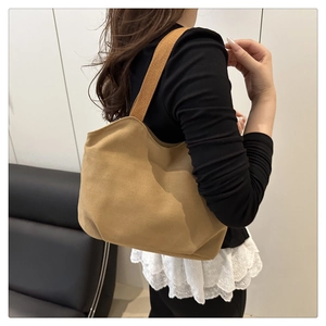 Detail view of a tan suede tote bag featuring thick woven shoulder straps on a model