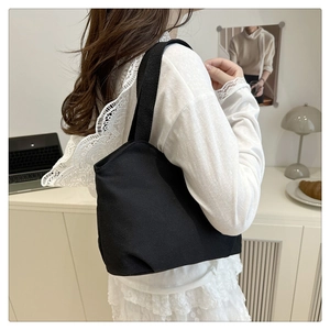 Detail shot of a black canvas tote bag worn with a white lace top in a modern setting