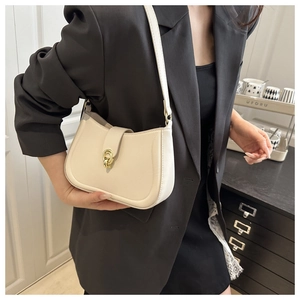 Detail of cream leather shoulder bag with gold hardware worn over a black blazer