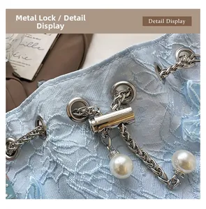 Detailed close-up of the silver metal clasp and faux pearl on the blue lace bucket bag