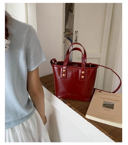 Detail of burgundy glossy leather bucket bag with gold studs and slender shoulder strap