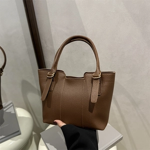 Sac à main minimaliste en cuir grainé marron foncé posé sur une table blanche