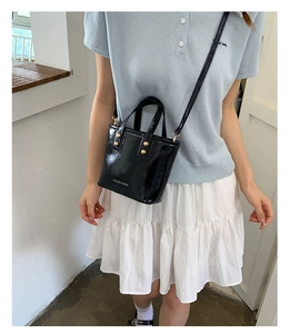 Detail of black patent leather tote bag with gold lettering and adjustable shoulder strap