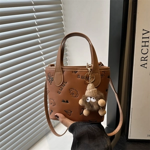 Brown bucket bag with embossed patterns and plush charm displayed in natural light