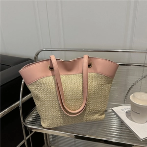 Pink leather and straw woven tote bag with metallic ring handles on a modern shelf
