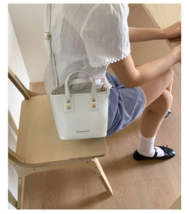 Detail of white mini bucket bag featuring gold stud accents and leather texture