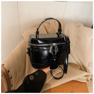 Macro detail of black patent leather box bag with circular handle and silver zipper