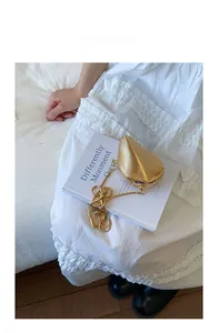 Detail of a golden leaf-shaped shell bag with wavy texture and gold chain on white fabric