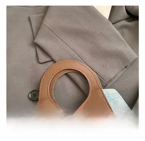 Detail of blue denim bucket bag with brown leather stitching and round cutout handle