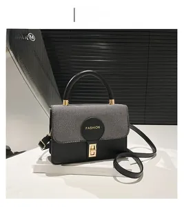 Detail of grey twill texture and golden twist-lock on a stylish black leather square bag