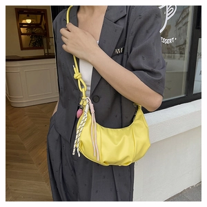 Close-up of bright yellow dumpling bag with knotted shoulder strap and heart pendant