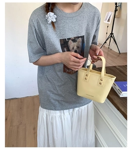 Detail of cream leather bucket bag with gold studs and fashion slogan on grey outfit