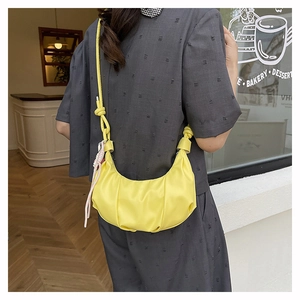 Detail view of yellow pleated crescent bag with knot strap on a person in a bakery cafe