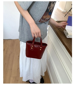 Close-up of wine red leather bucket bag with gold rivets held by a model in casual outfit
