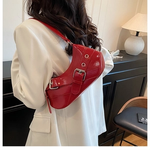 Close-up of red patent leather saddle bag featuring silver metal buckle details and grommets