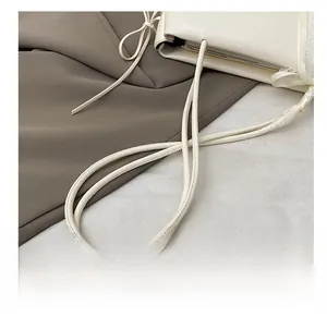 Détail d'un sac à main en cuir crème avec texture lisse et fine bandoulière arrondie élégante