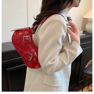 Detail view of red patent leather saddle bag with silver buckles and metallic eyelets
