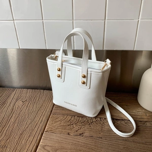 Elegant white bucket bag with gold studs and shoulder strap on a rustic wood surface
